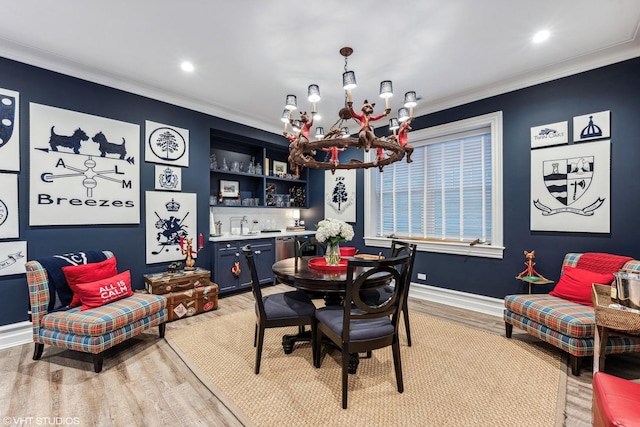 dining space with a chandelier, ornamental molding, light wood-style flooring, bar area, and baseboards