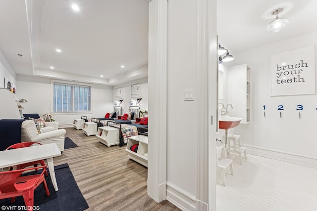 living room featuring a raised ceiling, baseboards, recessed lighting, and wood finished floors