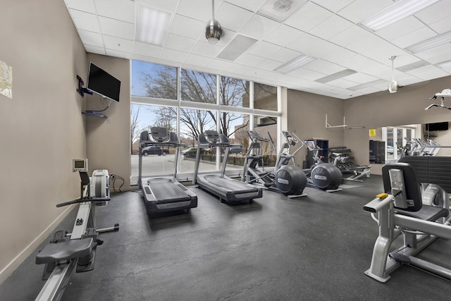 gym with a wall of windows, a paneled ceiling, and baseboards