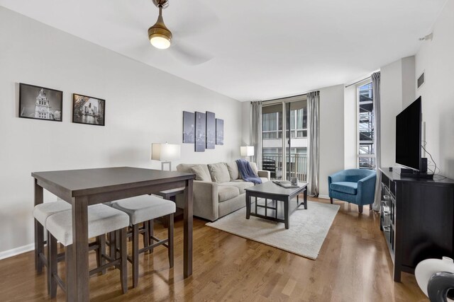 living area featuring ceiling fan, a wall of windows, visible vents, wood finished floors, and baseboards