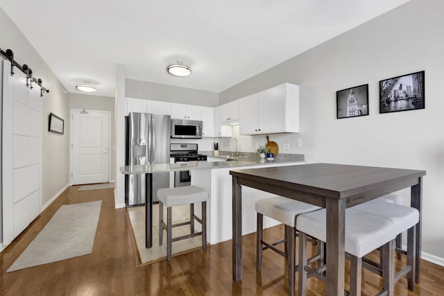 kitchen featuring a peninsula, white cabinetry, a barn door, appliances with stainless steel finishes, and wood finished floors
