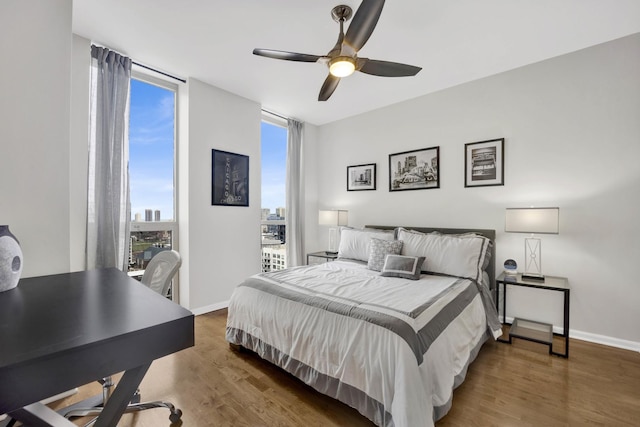 bedroom with a city view, wood finished floors, baseboards, and a wall of windows