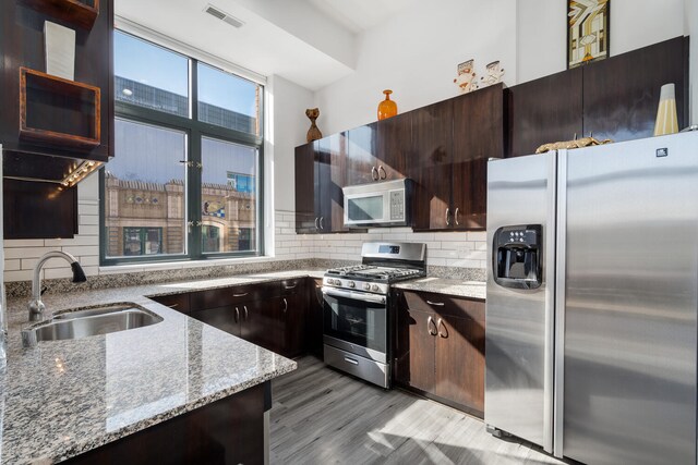 kitchen with visible vents, decorative backsplash, light stone countertops, a sink, and stainless steel appliances