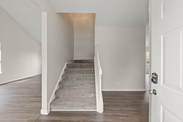 staircase featuring baseboards, wood finished floors, and lofted ceiling