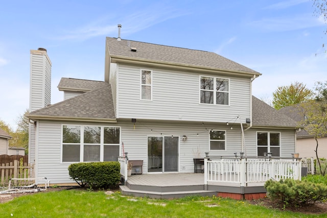 rear view of property with a lawn, a deck, fence, and roof with shingles