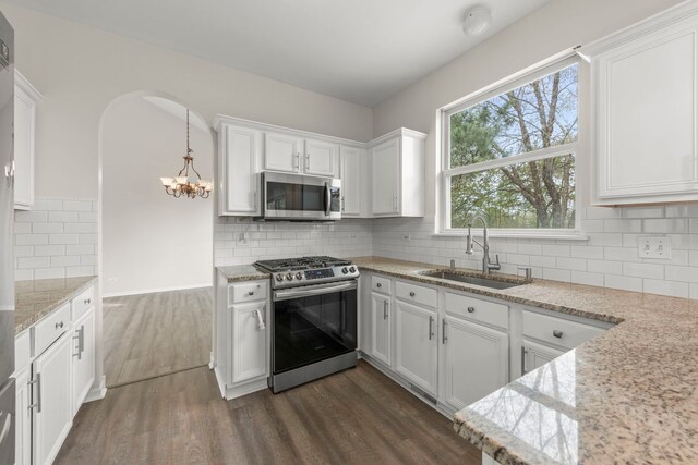kitchen featuring dark wood-style flooring, white cabinetry, a chandelier, a sink, and appliances with stainless steel finishes