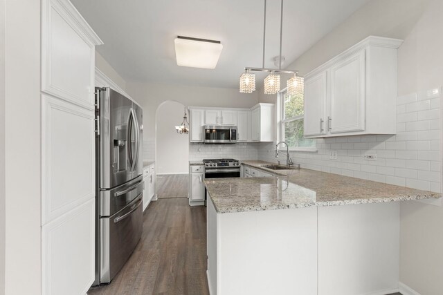kitchen with appliances with stainless steel finishes, light stone counters, a peninsula, backsplash, and dark wood-style floors