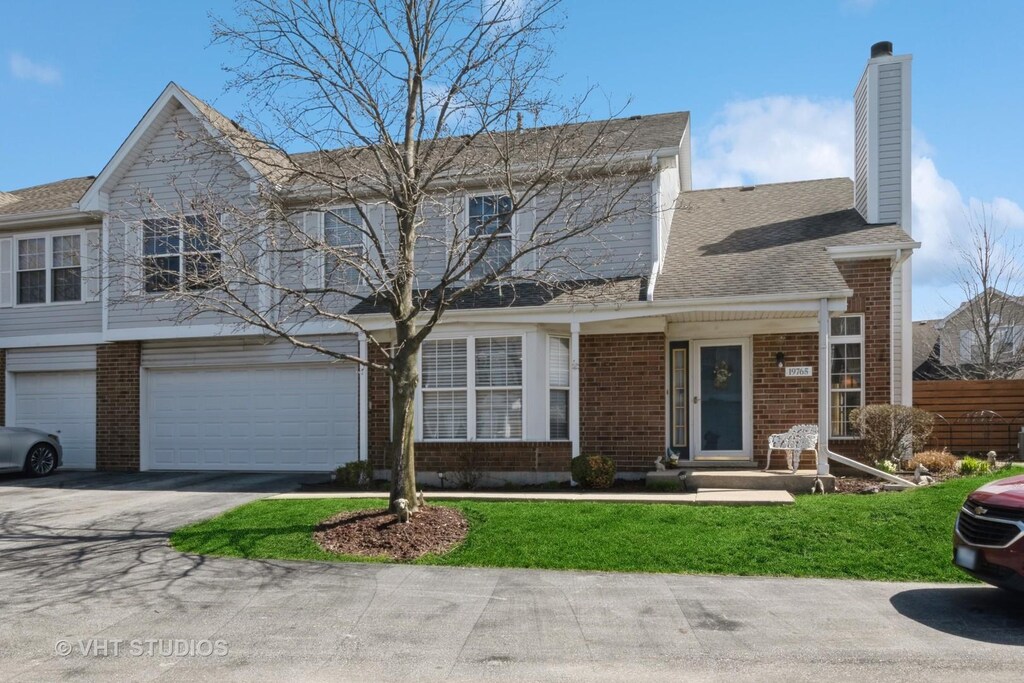 view of front of property featuring a chimney, driveway, an attached garage, a front lawn, and brick siding