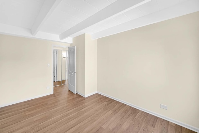 spare room with light wood-style floors, baseboards, and beamed ceiling