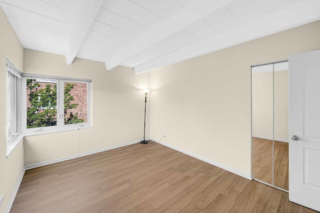 unfurnished bedroom with a closet, beam ceiling, baseboards, and wood finished floors