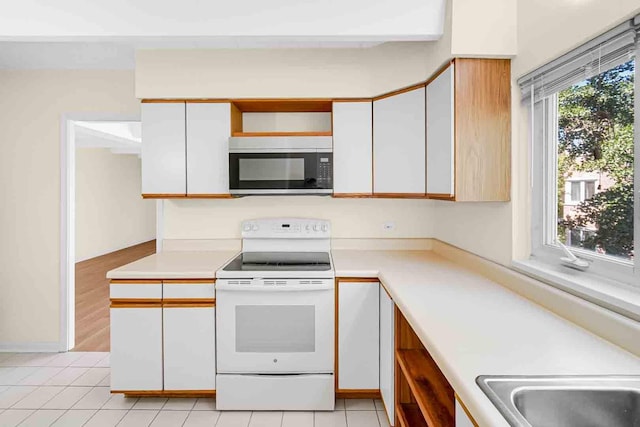 kitchen featuring stainless steel microwave, light countertops, white cabinetry, and electric range