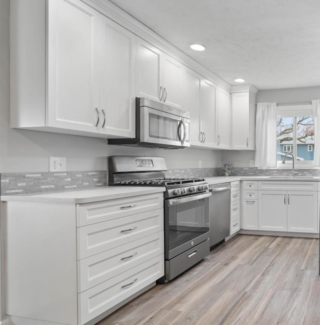 kitchen featuring light wood-style floors, white cabinetry, light countertops, a sink, and stainless steel appliances