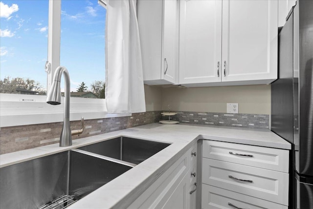 kitchen featuring freestanding refrigerator, light stone countertops, white cabinetry, a sink, and decorative backsplash