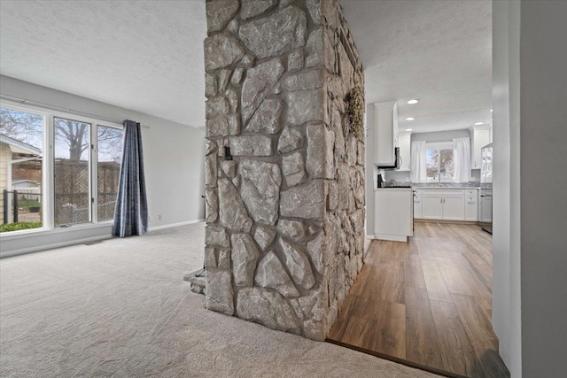 corridor featuring a textured ceiling, light colored carpet, recessed lighting, a sink, and baseboards