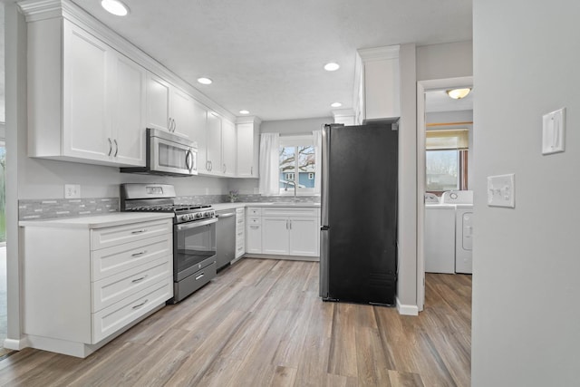kitchen with stainless steel appliances, light wood-type flooring, washing machine and dryer, and white cabinets