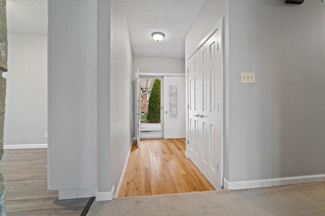 hall featuring a textured ceiling, wood finished floors, and baseboards