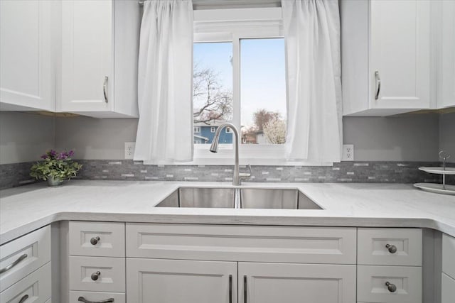 kitchen with a sink, white cabinets, and light stone counters