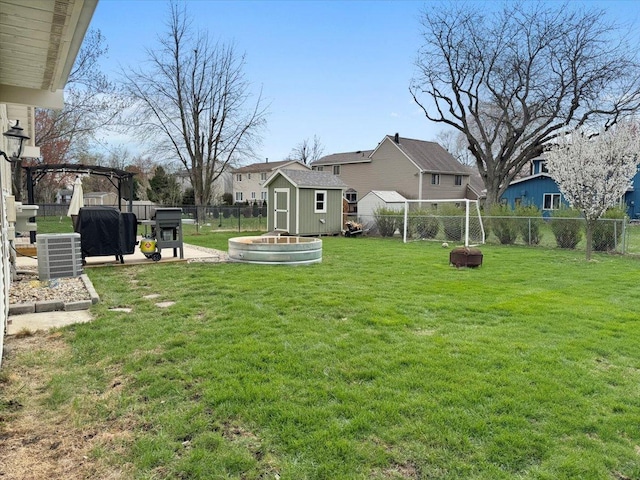 view of yard with central AC, a fenced backyard, an outdoor structure, a storage unit, and a residential view
