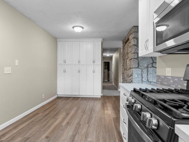 kitchen featuring stainless steel microwave, black range with gas cooktop, light wood-style flooring, white cabinetry, and backsplash