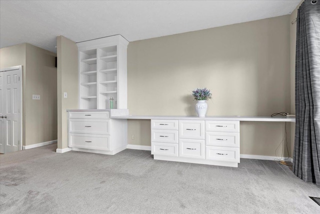 unfurnished office with light colored carpet, built in study area, and baseboards