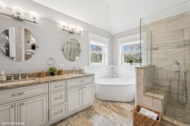 full bath featuring a sink, a wainscoted wall, tiled shower, and a soaking tub