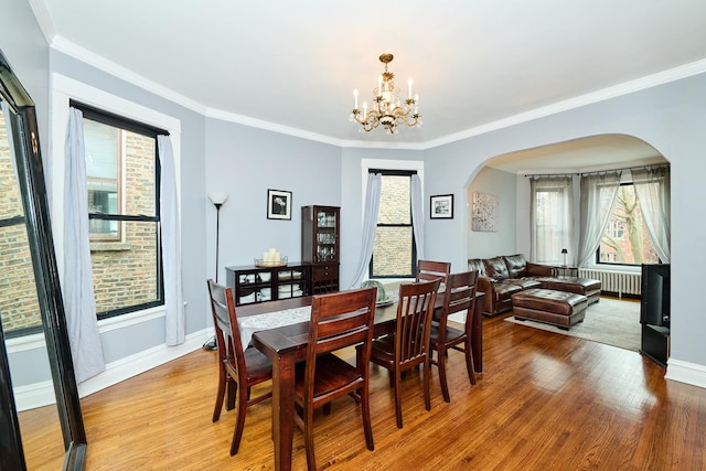 dining room with baseboards, wood finished floors, arched walkways, radiator, and a notable chandelier