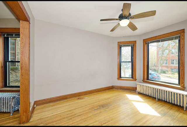 spare room with radiator, light wood-style floors, baseboards, and a ceiling fan