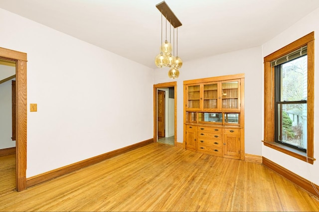 spare room with an inviting chandelier, light wood-style flooring, and baseboards