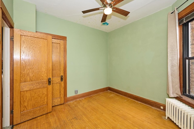 unfurnished bedroom featuring radiator, baseboards, ceiling fan, and light wood-type flooring