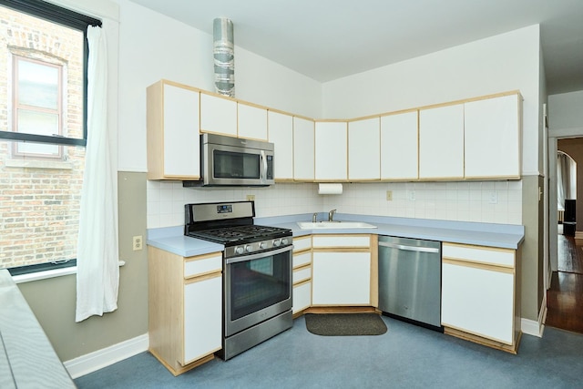 kitchen with light countertops, a sink, backsplash, stainless steel appliances, and baseboards
