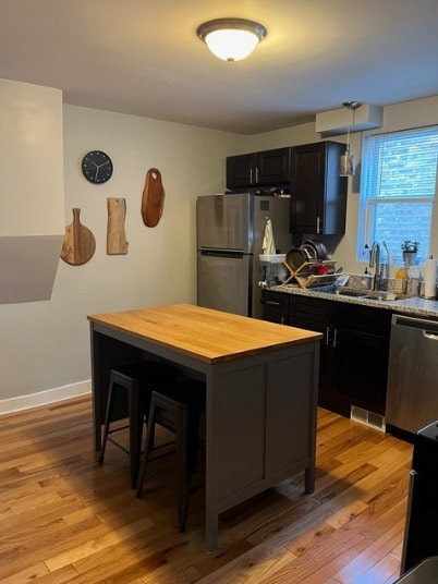 1516 W 18th Pl, Chicago, IL 60608 - kitchen with light wood-style floors, a breakfast bar, appliances with stainless steel finishes, dark cabinetry, and wood counters