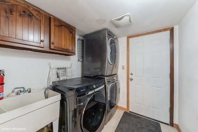 laundry room featuring stacked washer / dryer, baseboards, a sink, cabinet space, and light tile patterned floors