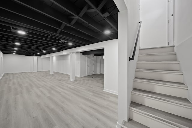 finished below grade area featuring baseboards, wood finished floors, and stairs