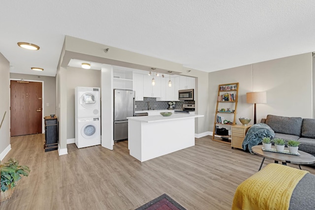 living room with estacked washer and dryer, baseboards, light wood-type flooring, and a textured ceiling