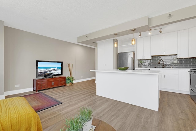 kitchen with freestanding refrigerator, light wood-style floors, light countertops, a center island, and backsplash