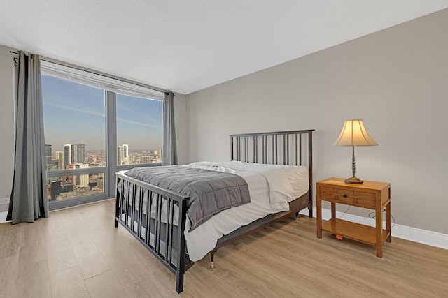 bedroom featuring floor to ceiling windows, light wood finished floors, and baseboards