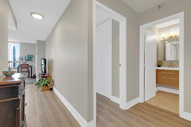 hall with light wood-type flooring, baseboards, and a sink