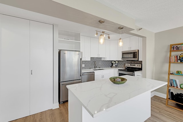 kitchen featuring appliances with stainless steel finishes, open shelves, a sink, light wood finished floors, and tasteful backsplash