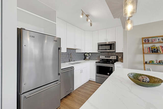 kitchen featuring stainless steel appliances, a sink, open shelves, and white cabinetry