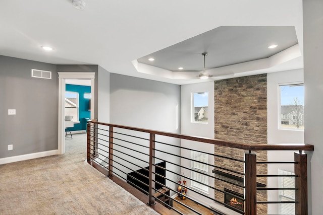 hallway featuring a tray ceiling, an upstairs landing, baseboards, visible vents, and recessed lighting