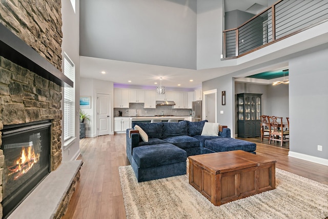 living room with a high ceiling, light wood-style flooring, a stone fireplace, and baseboards
