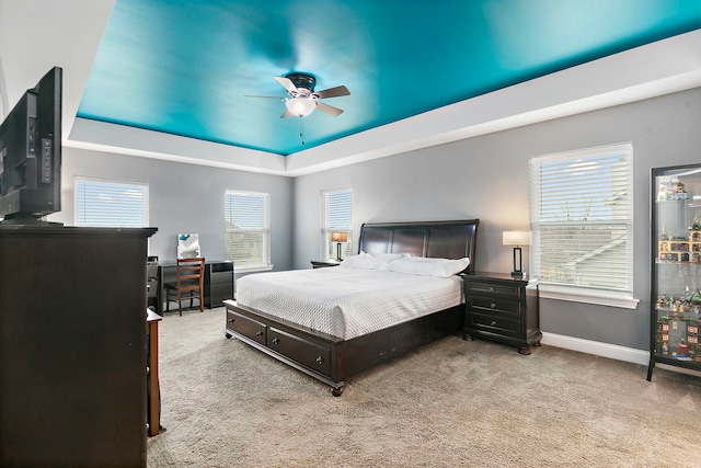 carpeted bedroom featuring a tray ceiling, baseboards, and ceiling fan