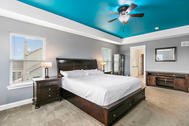 carpeted bedroom featuring baseboards, ceiling fan, ensuite bathroom, and a tray ceiling