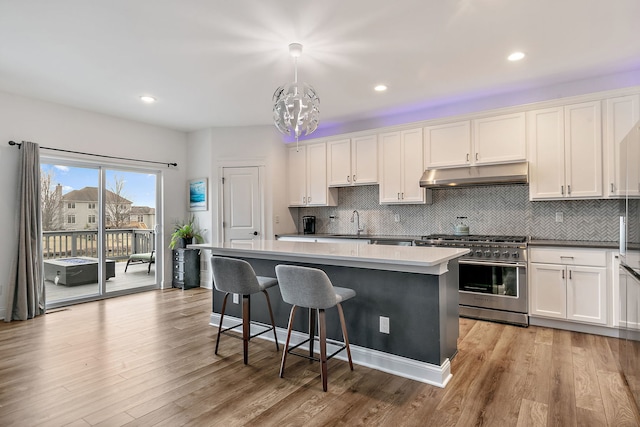 kitchen featuring white cabinets, light wood finished floors, high end stainless steel range oven, under cabinet range hood, and a center island