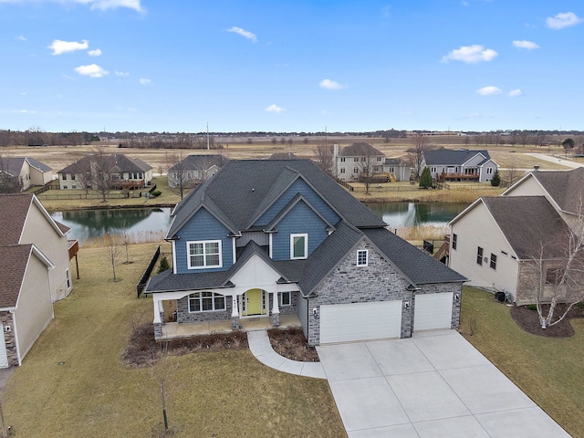 view of front of home with roof with shingles, stone siding, a water view, driveway, and a front lawn