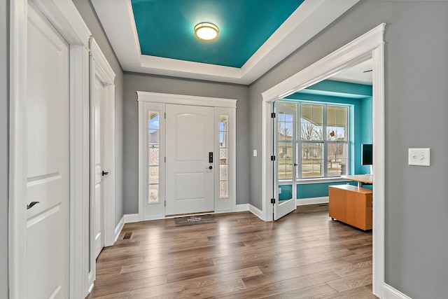 entryway with a raised ceiling, visible vents, baseboards, and wood finished floors