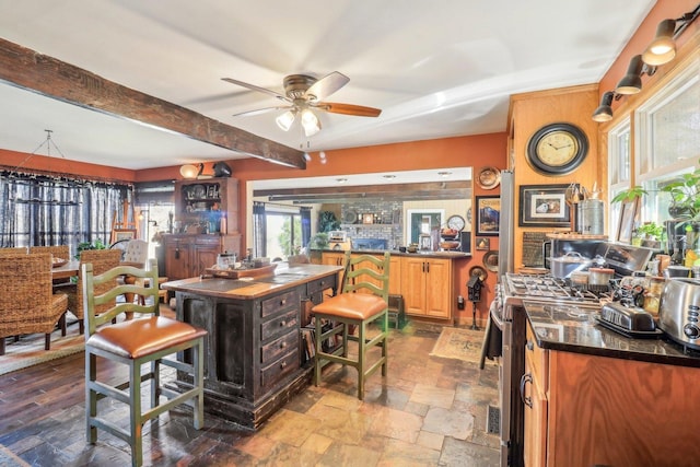 kitchen with stone tile flooring, a ceiling fan, gas range, dark countertops, and beam ceiling