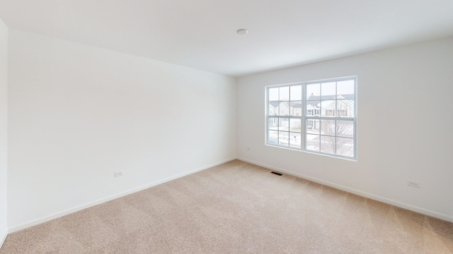 spare room featuring visible vents, light colored carpet, and baseboards