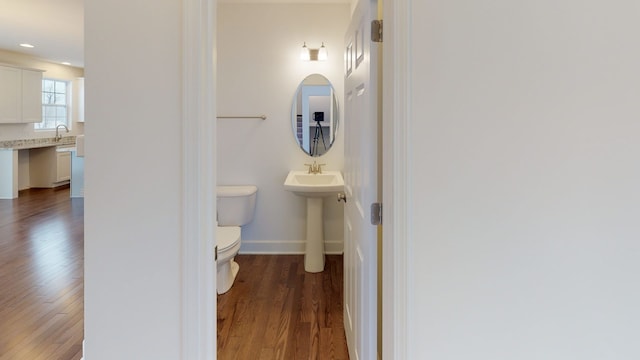 half bath with a sink, toilet, wood finished floors, and baseboards