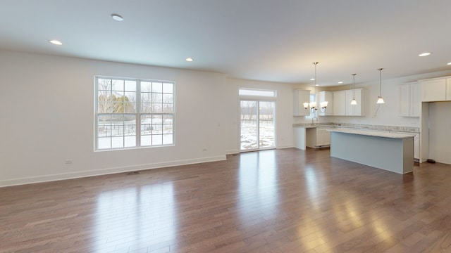 unfurnished living room featuring recessed lighting, a sink, a notable chandelier, dark wood-style floors, and baseboards